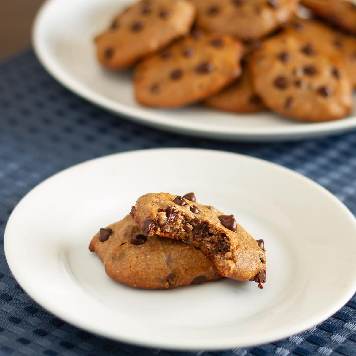 plate with two no flour cookies with a bite taken off showing the inside and more cookies plated in the background