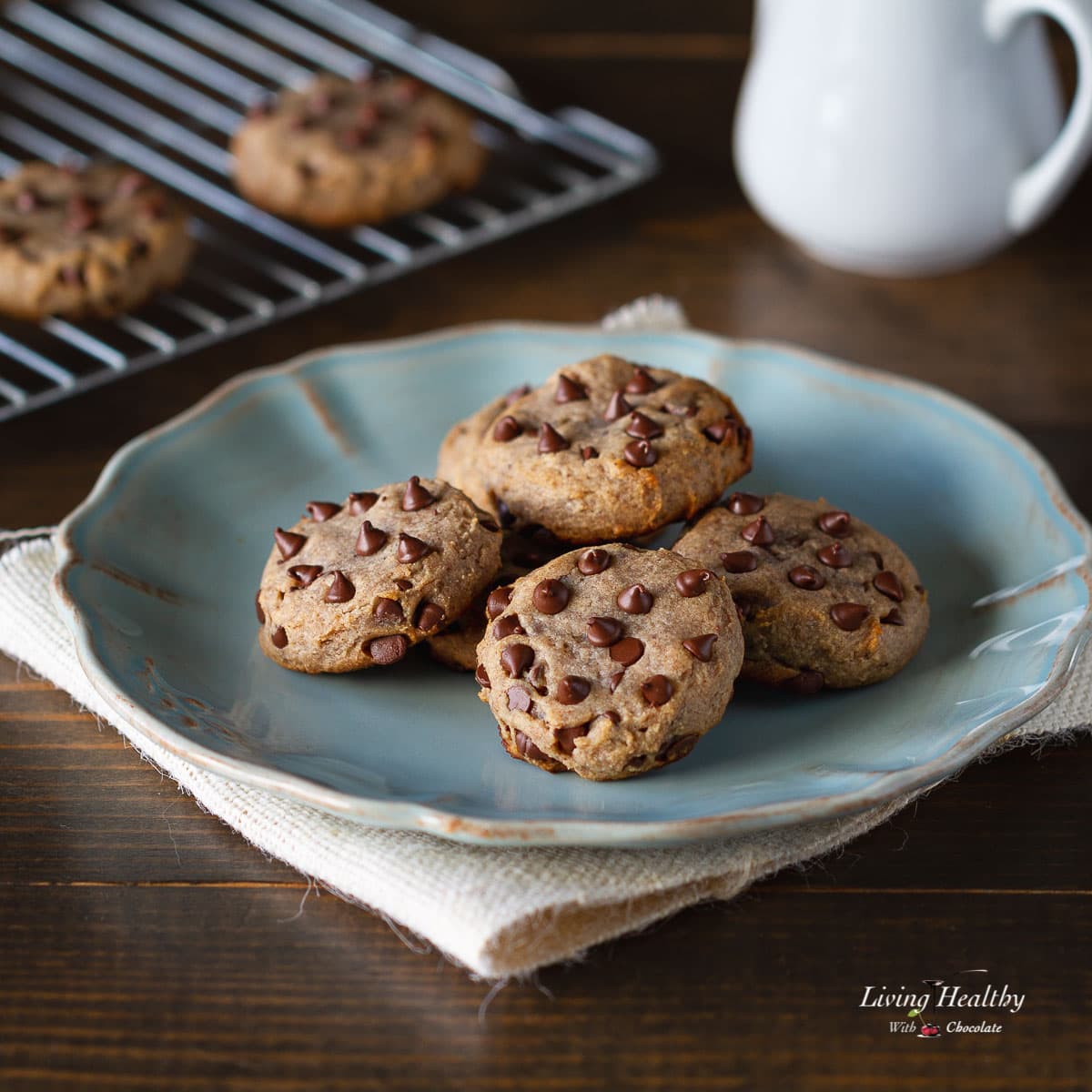 numerous paleo flourless chocolate chip cookies on a white plate with blue placemat underneath 