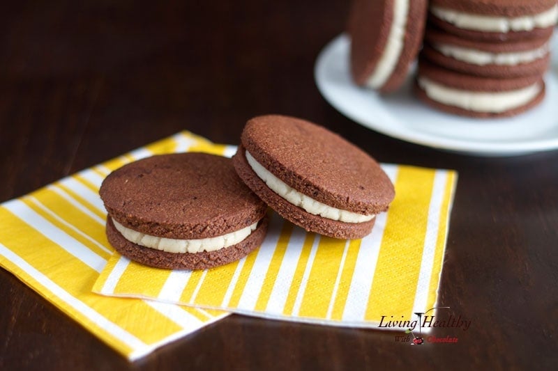 two homemade oreo cookies on yellow napkin in foreground with plate of more cookies in background 