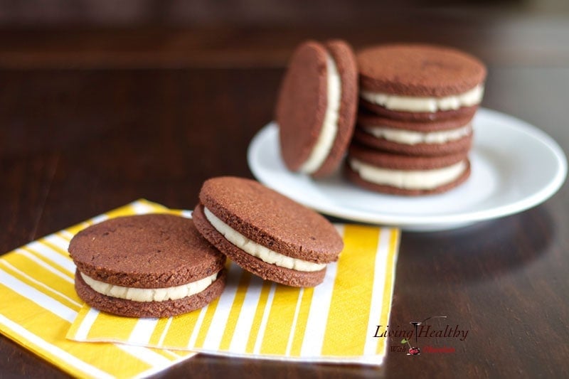 two homemade oreo cookies on yellow napkin in foreground with plate of more cookies in background 