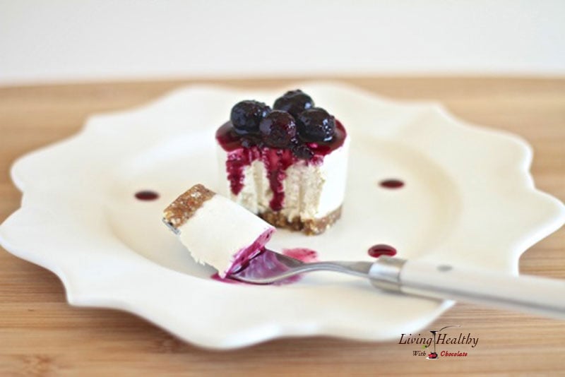 plate with a single serving raw no bake blueberry cheesecake topped with blueberries and fork with one bite in foreground 