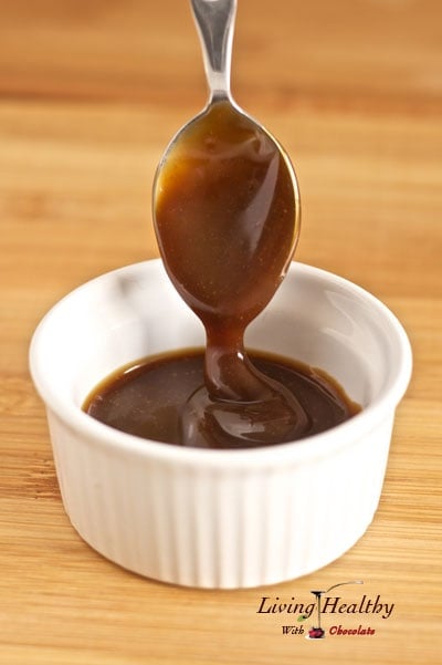 close up of a small white dish filled with homemade Caramel sauce with a spoon dripping sauce from above