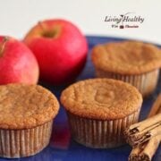 three apple cinnamon muffins on a blue plate with two red apples in background and sticks of cinnamon in foreground