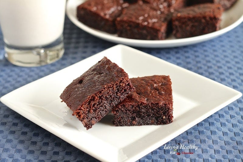 two paleo gluten free brownies with plate of more brownies and glass of milk in background 