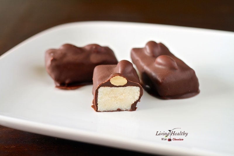 close up of homemade almond joy candy pieces on white plate with one cut in half showing the middle