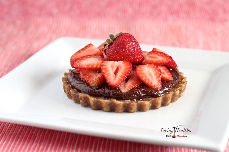 close up of homemade paleo nutella strawberry tart topped with slices of fresh strawberries and chocolate ganache 