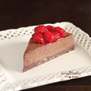 single slice of raspberry chocolate truffle pie topped with fresh raspberries on a white square plate with dark background
