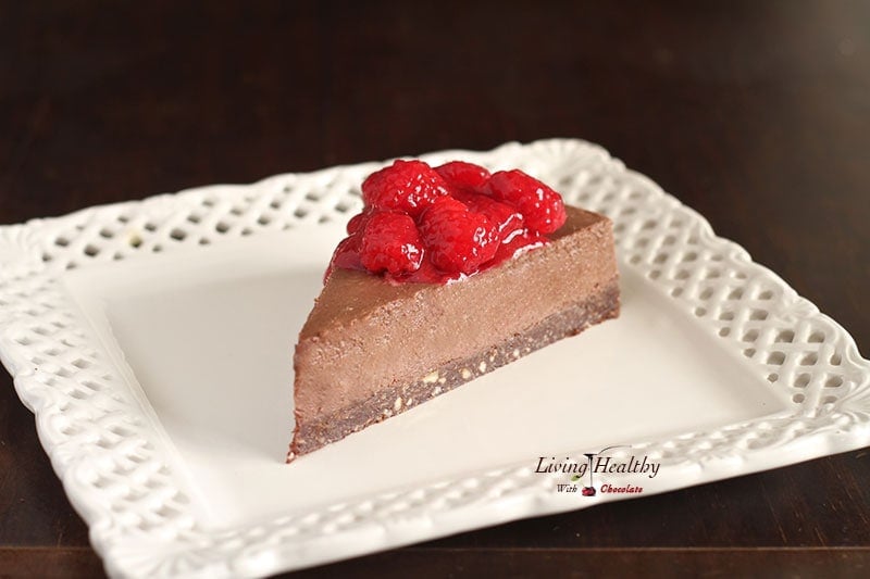 single slice of raspberry chocolate truffle pie topped with fresh raspberries on a white square plate with dark background 