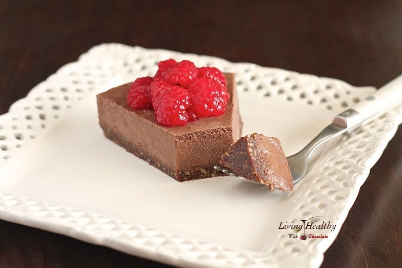 single slice of raspberry chocolate truffle pie topped with fresh raspberries on a white square plate with dark background 
