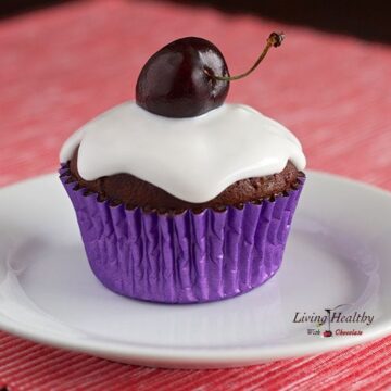 close up of paleo red velvet chocolate cherry cupcake topped with white frosting and one single cherry