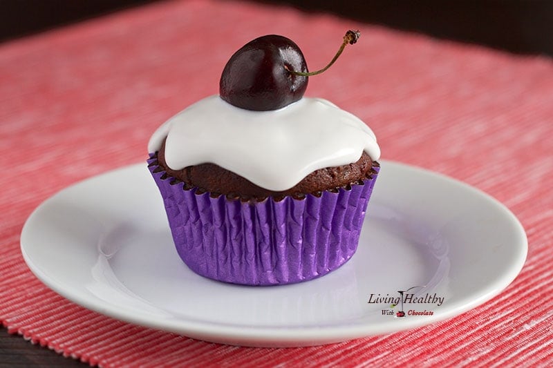 close up of paleo red velvet chocolate cherry cupcake topped with white frosting and one single cherry