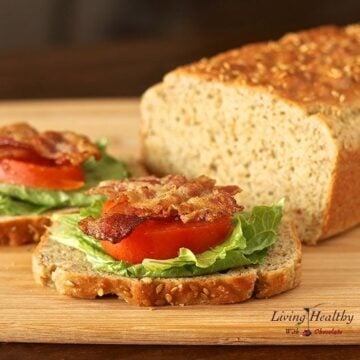 loaf of homemade paleo sandwich bread on cutting board with two slices topped with bacon lettuce and tomato