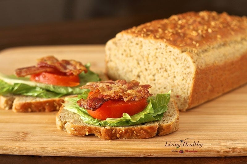 loaf of homemade paleo sandwich bread on cutting board with two slices topped with bacon lettuce and tomato