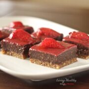 plate with several squares of paleo strawberry chocolate fudge cookie bars topped slice of strawberry