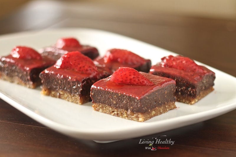 plate with several squares of paleo strawberry chocolate fudge cookie bars topped slice of strawberry