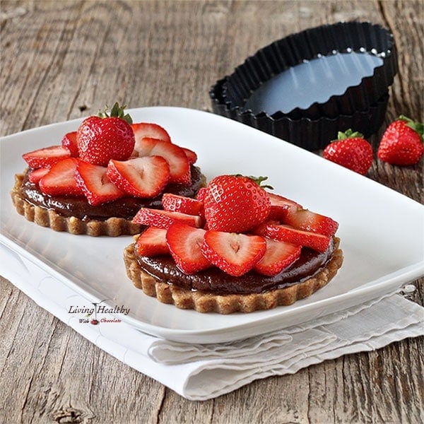 two homemade paleo nutella strawberry tarts topped with slices of fresh strawberries and chocolate ganache 