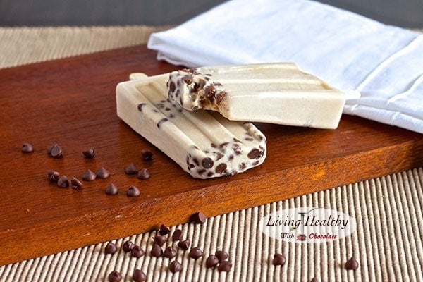 wooden board with two chocolate chip cookie dough popsicles with loose chocolate chips in foreground 