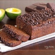 loaf of paleo avocado chocolate bread topped with loads of chocolate chips and more chocolate and avocado in background