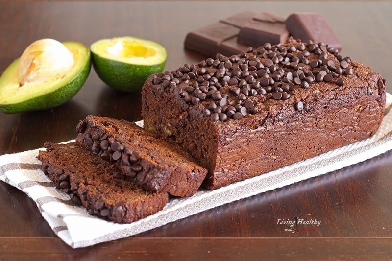 loaf of paleo avocado chocolate bread topped with loads of chocolate chips and more chocolate and avocado in background 