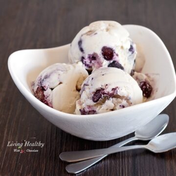 bowl of blueberry cheesecake ice cream on a wooden table with two silver spoons in front of bowl