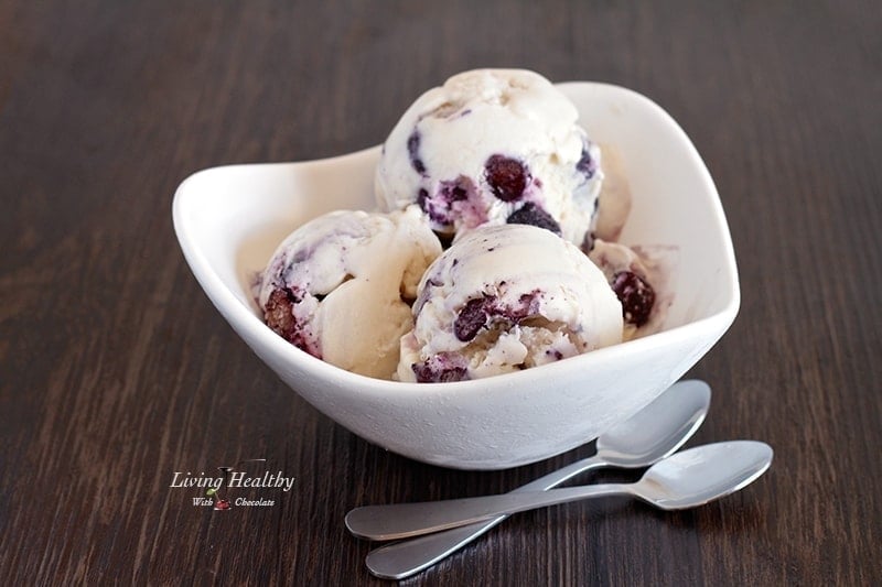 bowl of blueberry cheesecake ice cream on a wooden table with two silver spoons in front of bowl