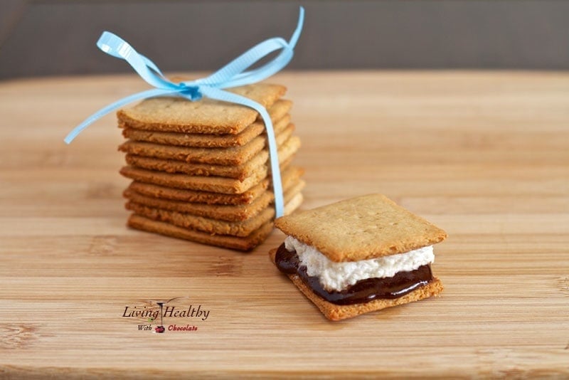 wooden cutting board with one paleo s'mores dessert treat with stack of homemade graham crackers with blue bow