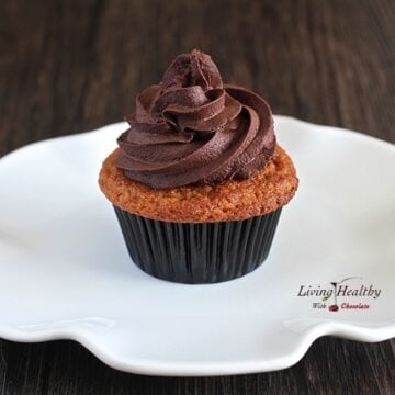 close up of a vanilla cupcake with chocolate banana frosting on a white plate sitting on a dark wooden table