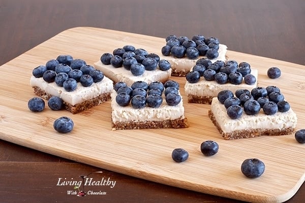 wooden cutting board topped with several pieces of blueberry coconut cream pie squares with lots of blueberries on top of each