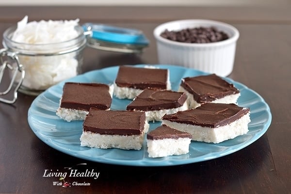 blue plate topped with numerous paleo coconut bark bars topped with chocolate and more chocolate and coconut in jars behind 