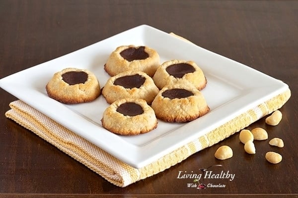 square plate with six paleo macadamia nut chocolate filled thumbprint cookies on wooden table