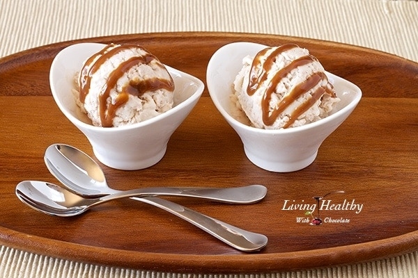 wooden serving tray with two small white dishes filled with toasted coconut caramel ice cream with two spoons in foreground 