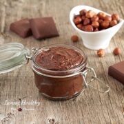 jar of homemade Nutella chocolate hazelnut spread with dish of hazelnuts in background and a few chocolate blocks