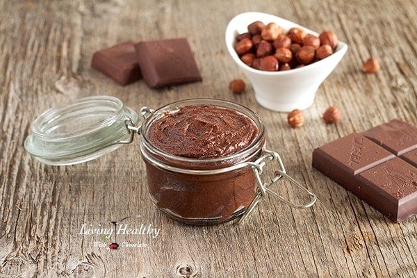 jar of homemade Nutella chocolate hazelnut spread with dish of hazelnuts in background and a few chocolate blocks