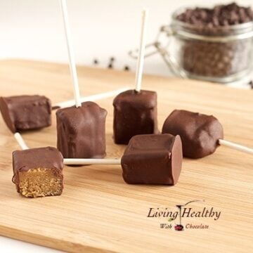 wooden cutting board with several chocolate covered peanut butter pops with jar of chocolate chips in background