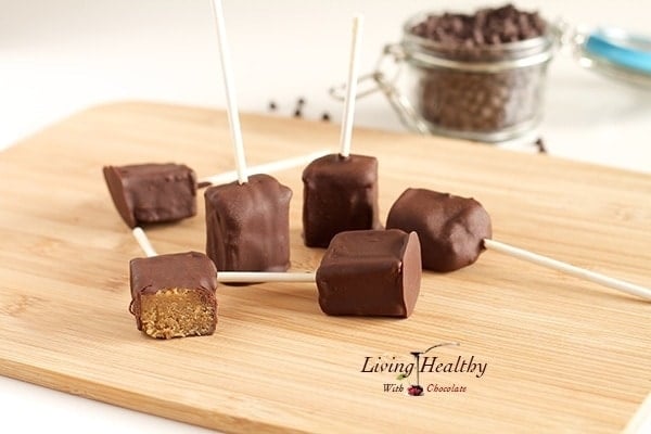wooden cutting board with several chocolate covered peanut butter pops with jar of chocolate chips in background 