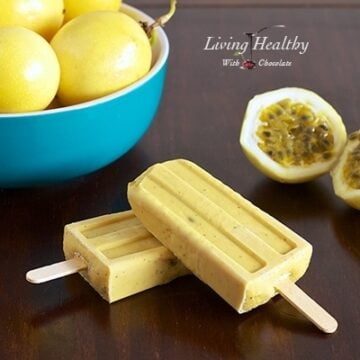wooden table with two paleo passion fruit popsicles in foreground and a bowl of passion fruit in background