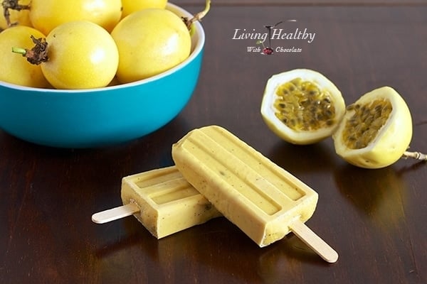 wooden table with two paleo passion fruit popsicles in foreground and a bowl of passion fruit in background