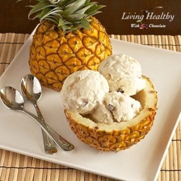 whole pineapple cut in half with one half filled with paleo pineapple coconut ice cream on white plate with two spoons
