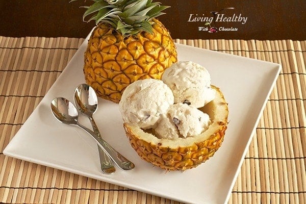 whole pineapple cut in half with one half filled with paleo pineapple coconut ice cream on white plate with two spoons  