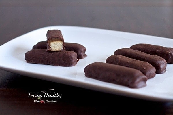 close up of homemade paleo twix cookie bars on white plate with one bar broken in half to show the middle