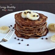 stack of paleo banana pancakes topped with slices of banana on a large white plate on wooden table