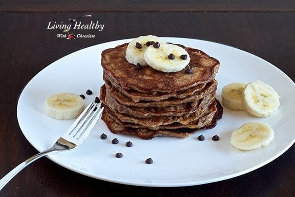 stack of paleo banana pancakes topped with slices of banana on a large white plate on wooden table