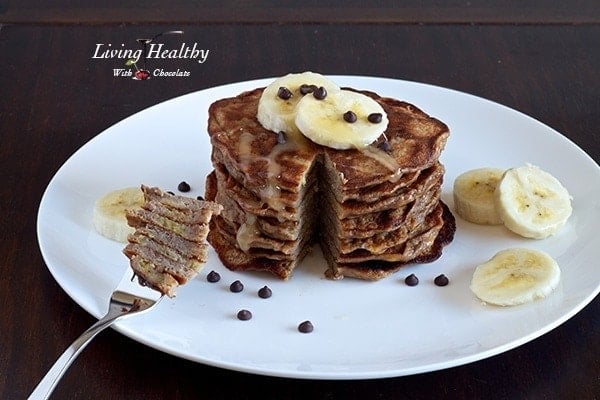 stack of paleo banana pancakes topped with slices of banana on a large white plate with bite taken out on fork