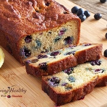 paleo blueberry bread loaf with lemon glaze on cutting board with loose blueberries in background