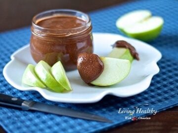jar of paleo chocolate almond butter with slices of green apple on plate with knife in foreground on blue placemat