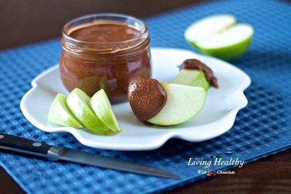 jar of paleo chocolate almond butter with slices of green apple on plate with knife in foreground on blue placemat