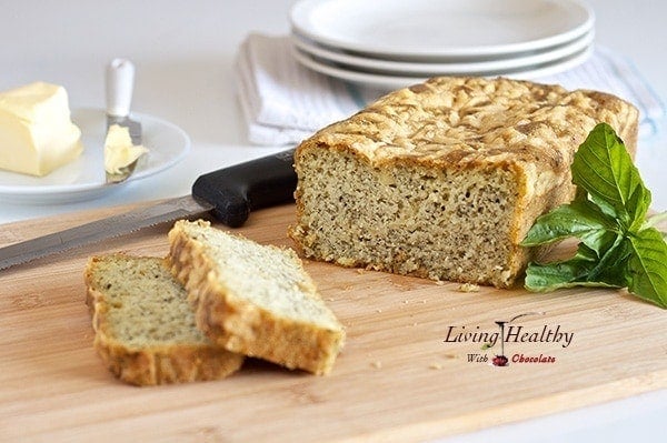 loaf of paleo pesto cheese bread with two slices cut on a cutting board with knife and plates in background 
