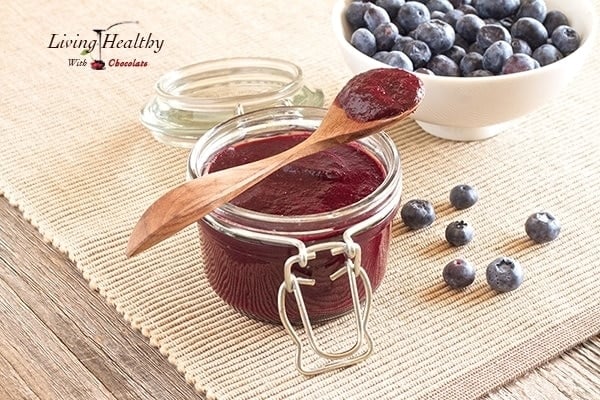 jar of homemade sugar free blueberry butter with wooden spoon on top and bowl of blueberries in background 