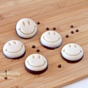 wooden table with five coconut smily treats with some loose chocolate chips scattered between the treats