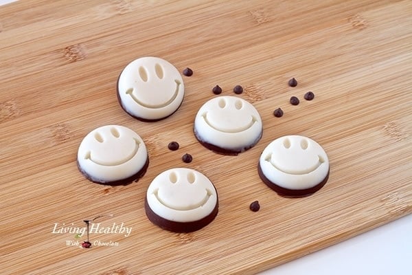 wooden table with five coconut smily treats with some loose chocolate chips scattered between the treats